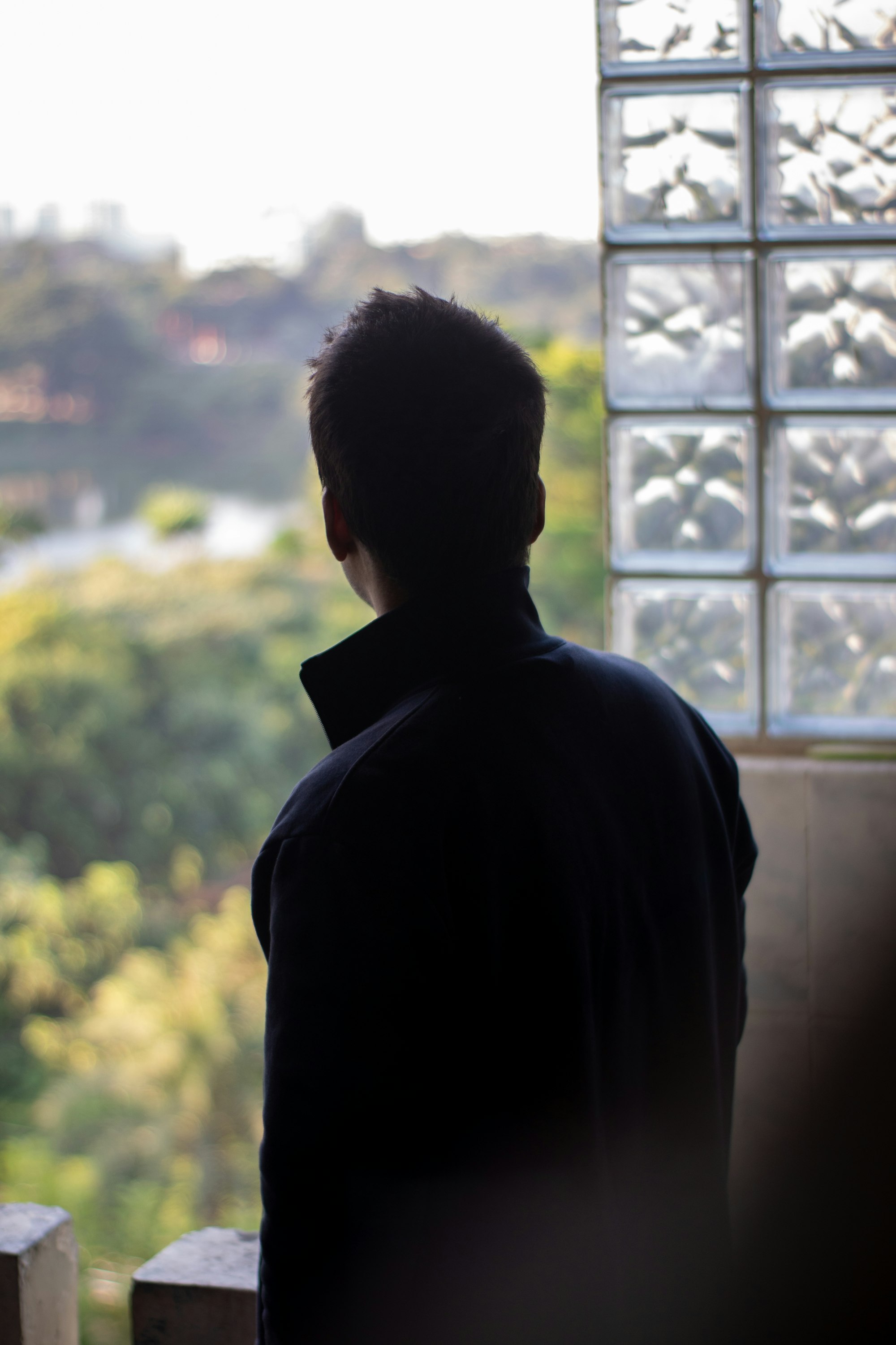 Man looking out a window at trees in quiet reflection