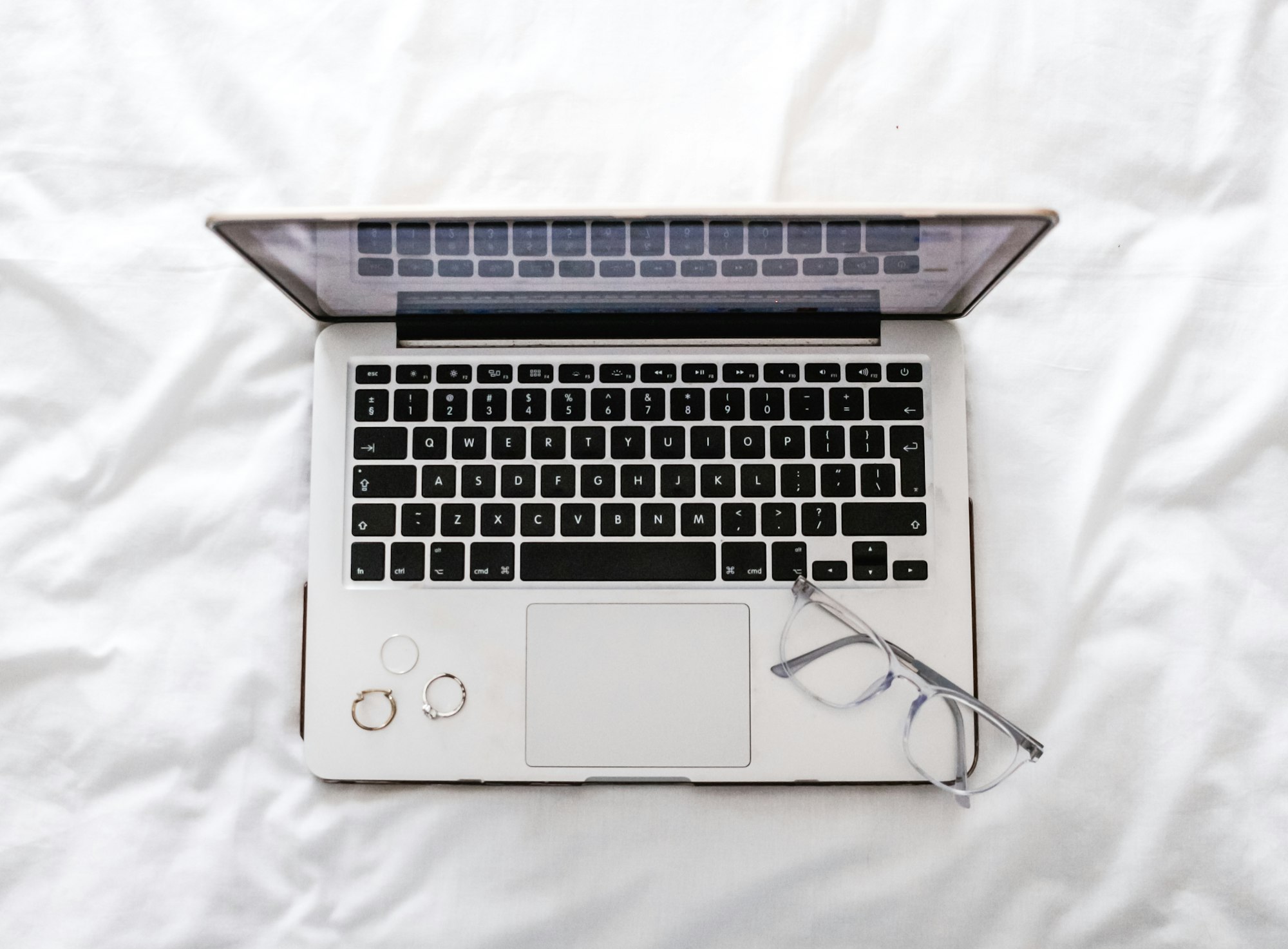 Laptop open on white sheets with glasses nearby