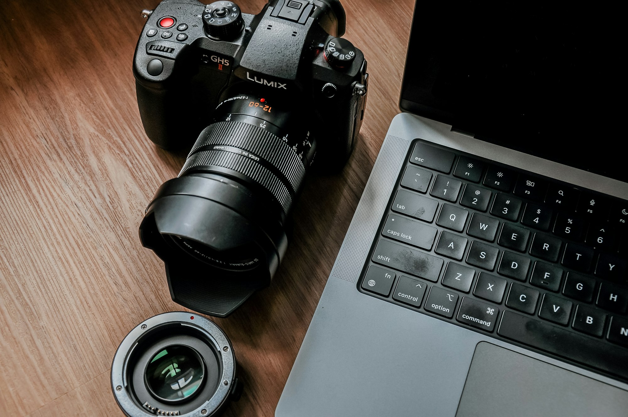 Camera and lens sitting next to a laptop on a wooden desk