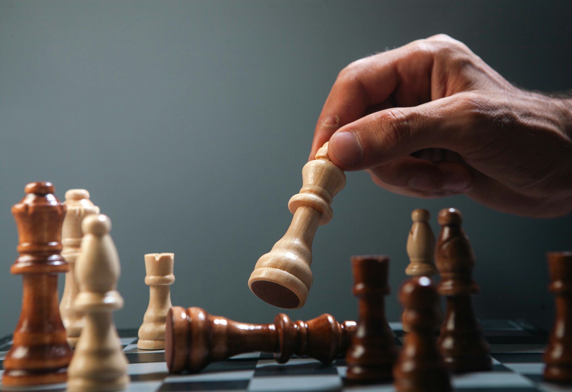 Hand moving a white chess piece over fallen king