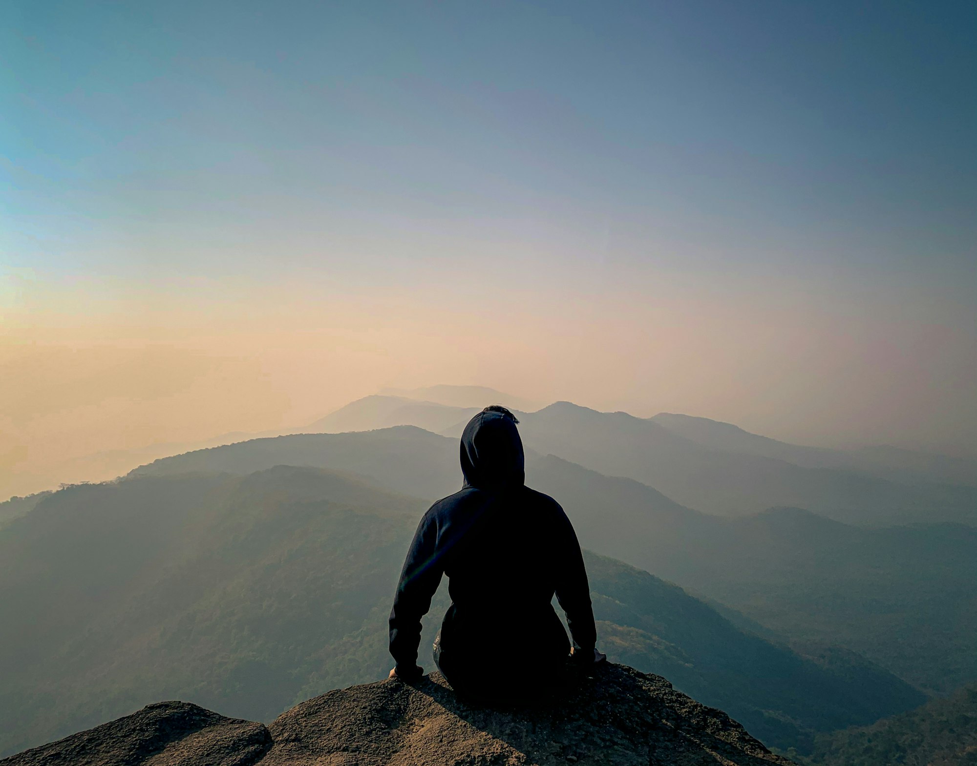 Person sitting on a mountain overlooking a calm valley