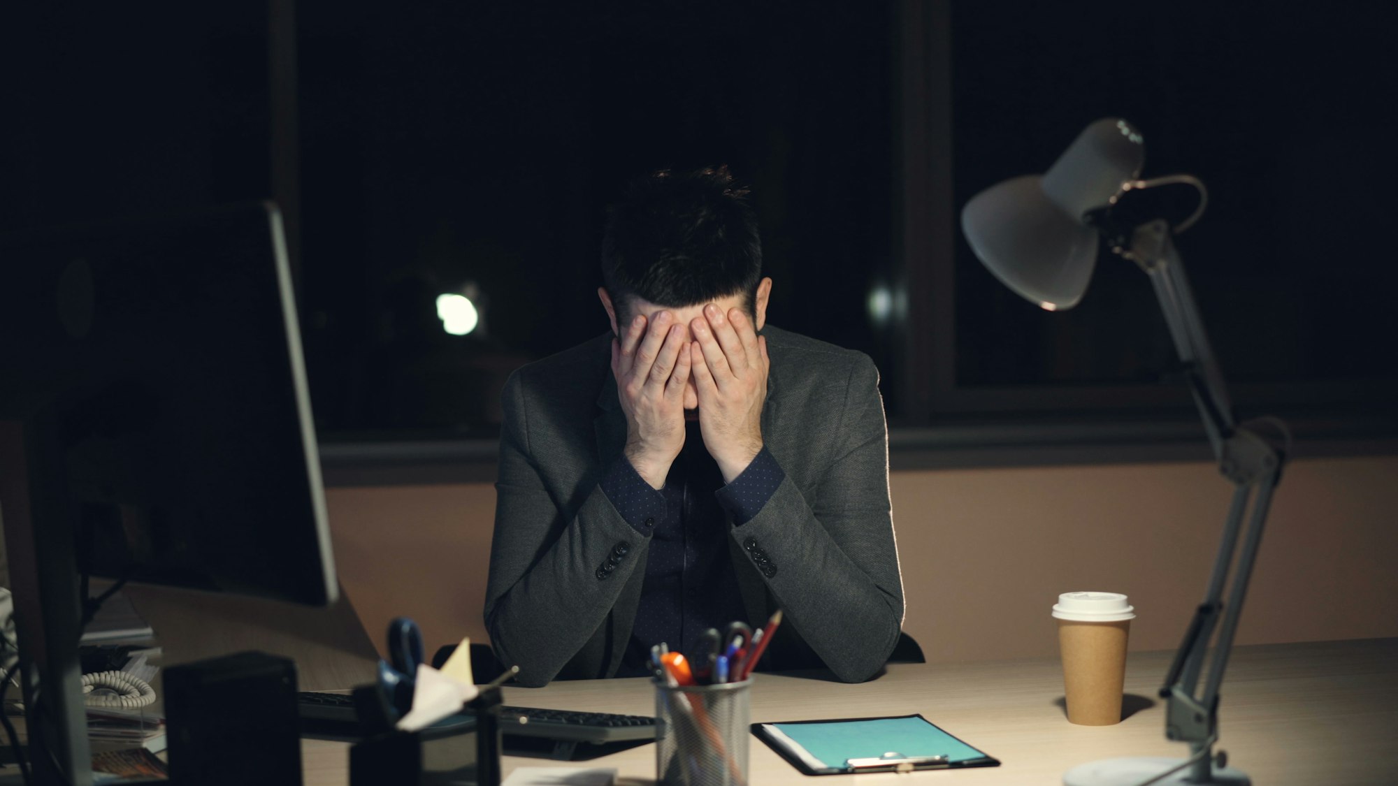 Man in suit sits at desk with head in hands