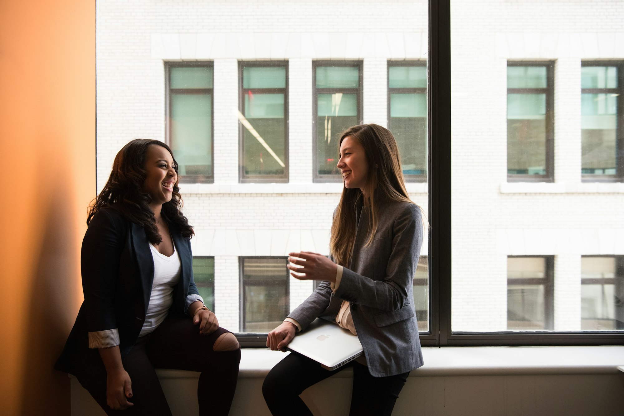 Two coworkers sitting by a window in conversation