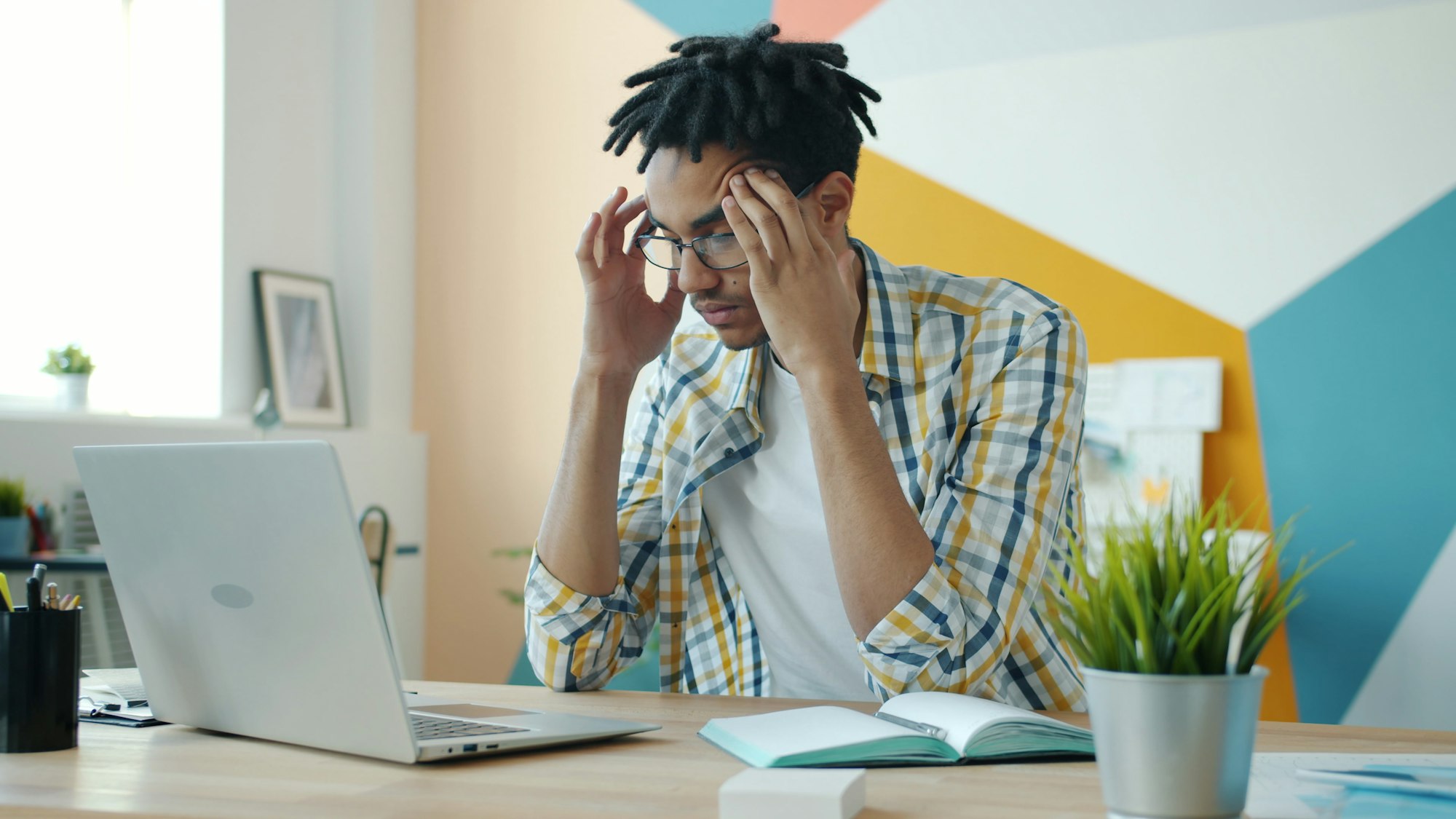 Man holding his head at desk with laptop, struggling with mental health