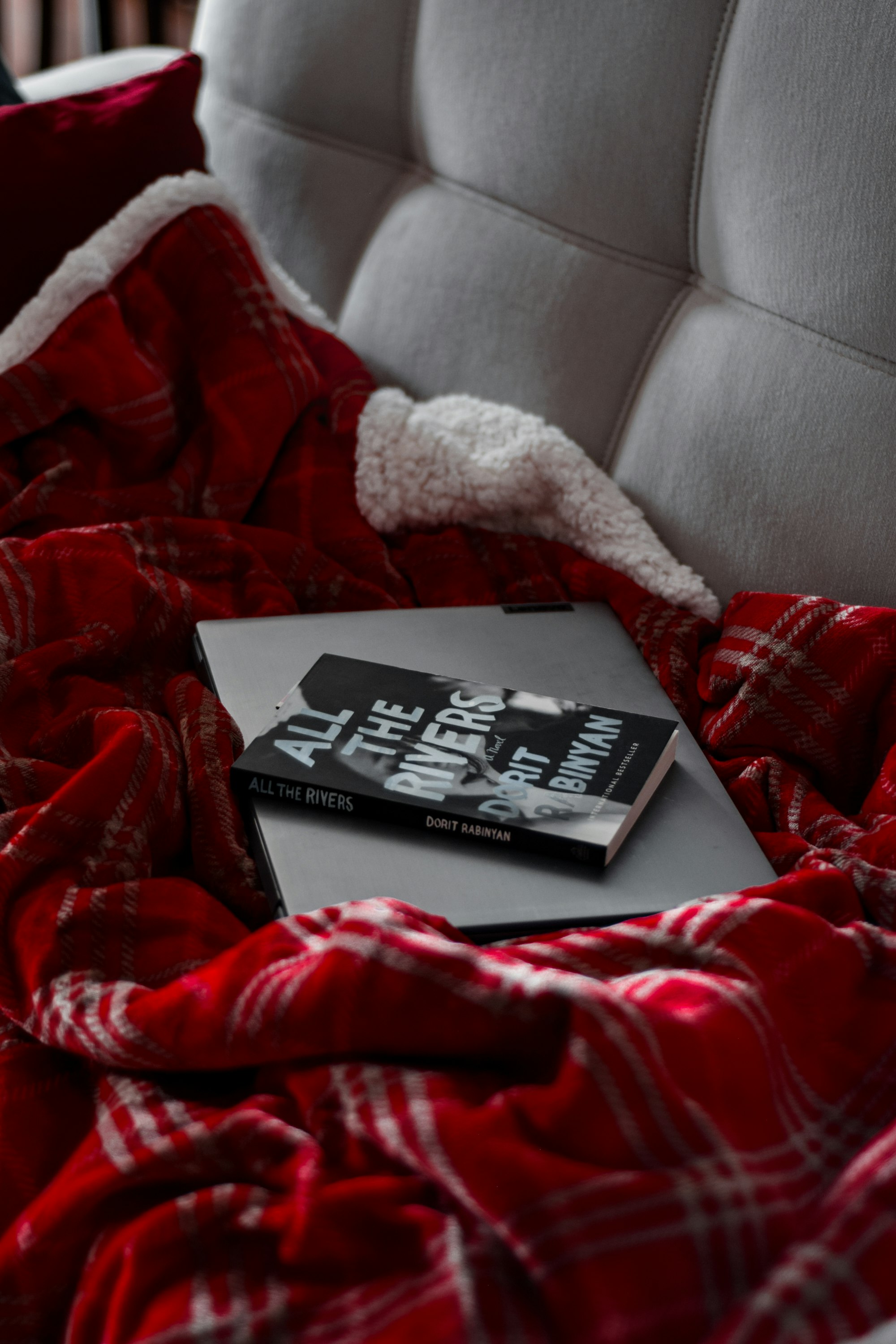 Book resting on a cozy red plaid blanket on a couch