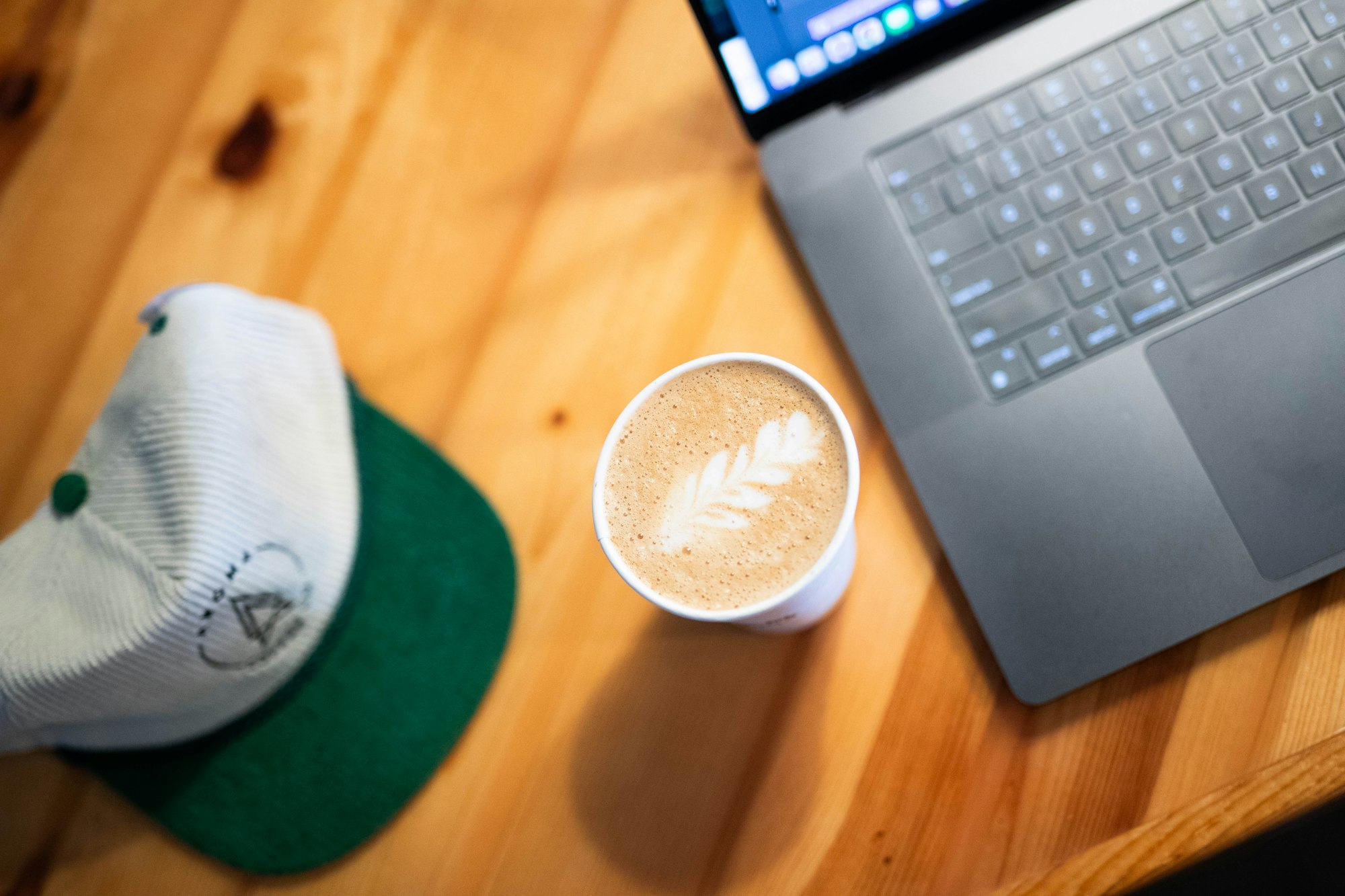 Laptop, coffee, and cap on a wooden table from above
