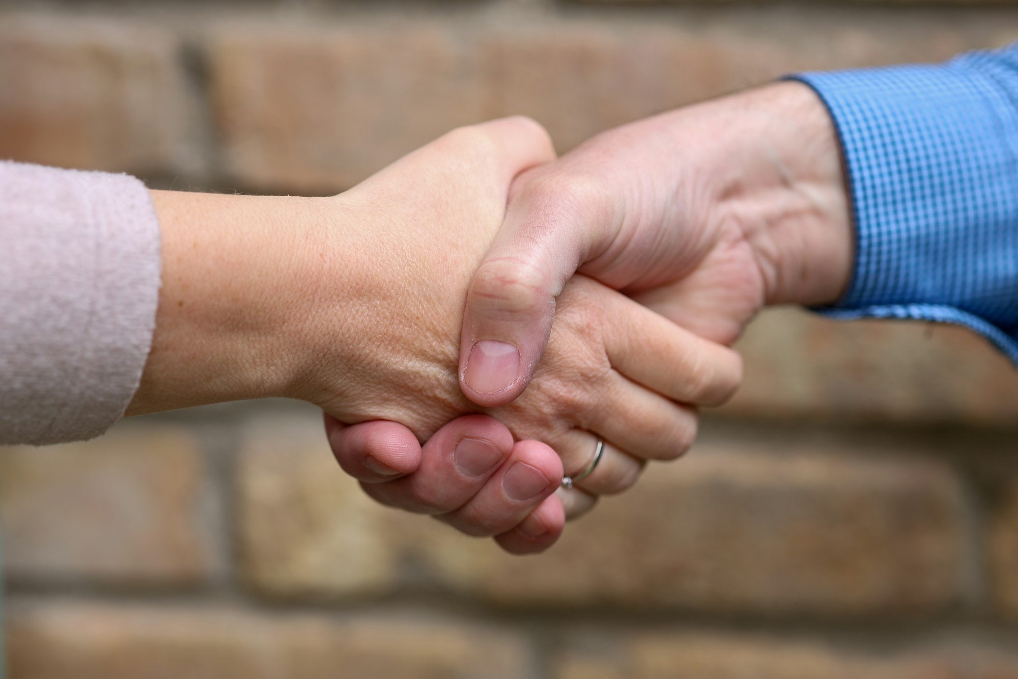 Two people shaking hands across a table with a coffee mug visible