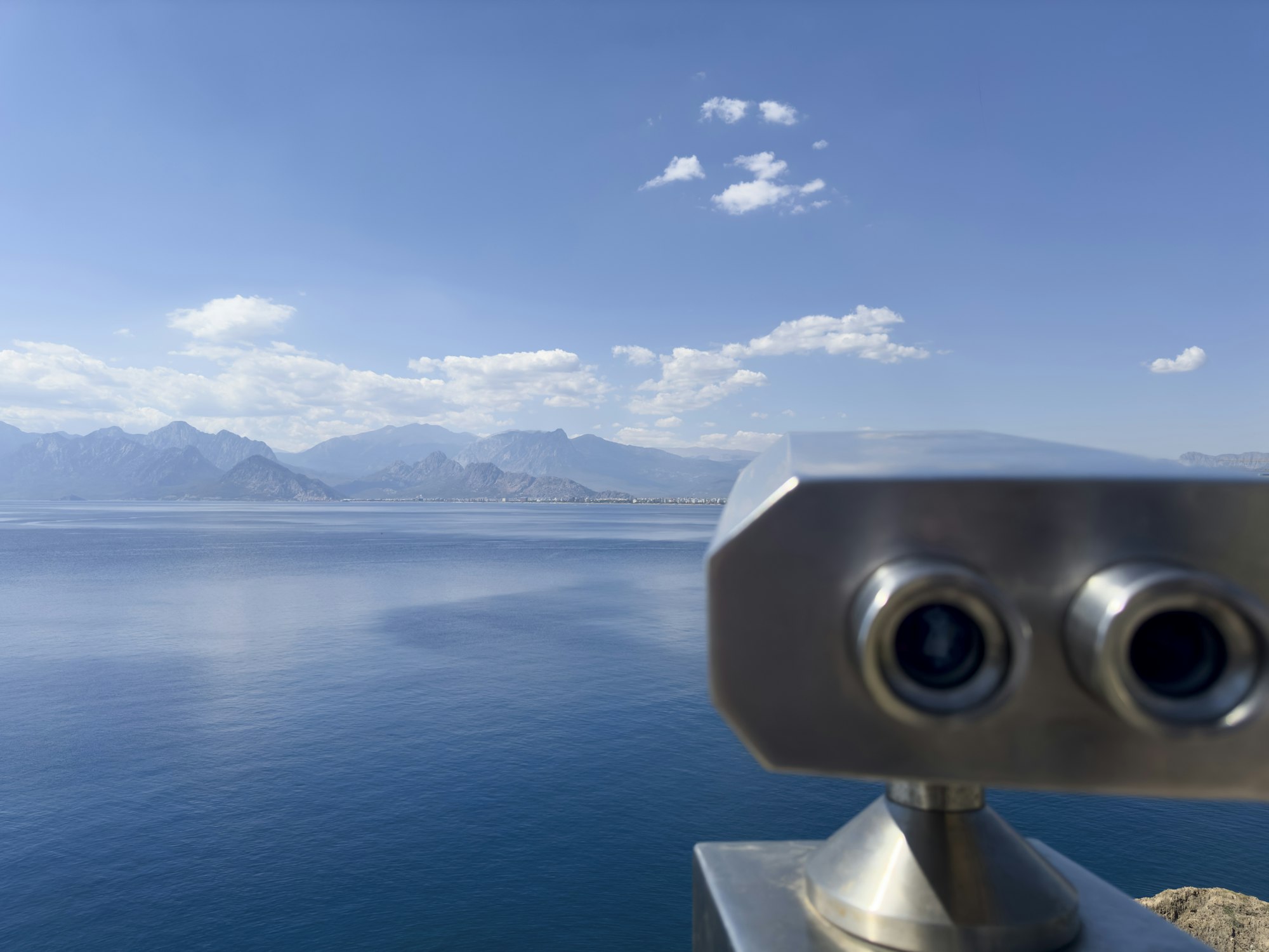 Binoculars overlooking a calm blue sea and mountains