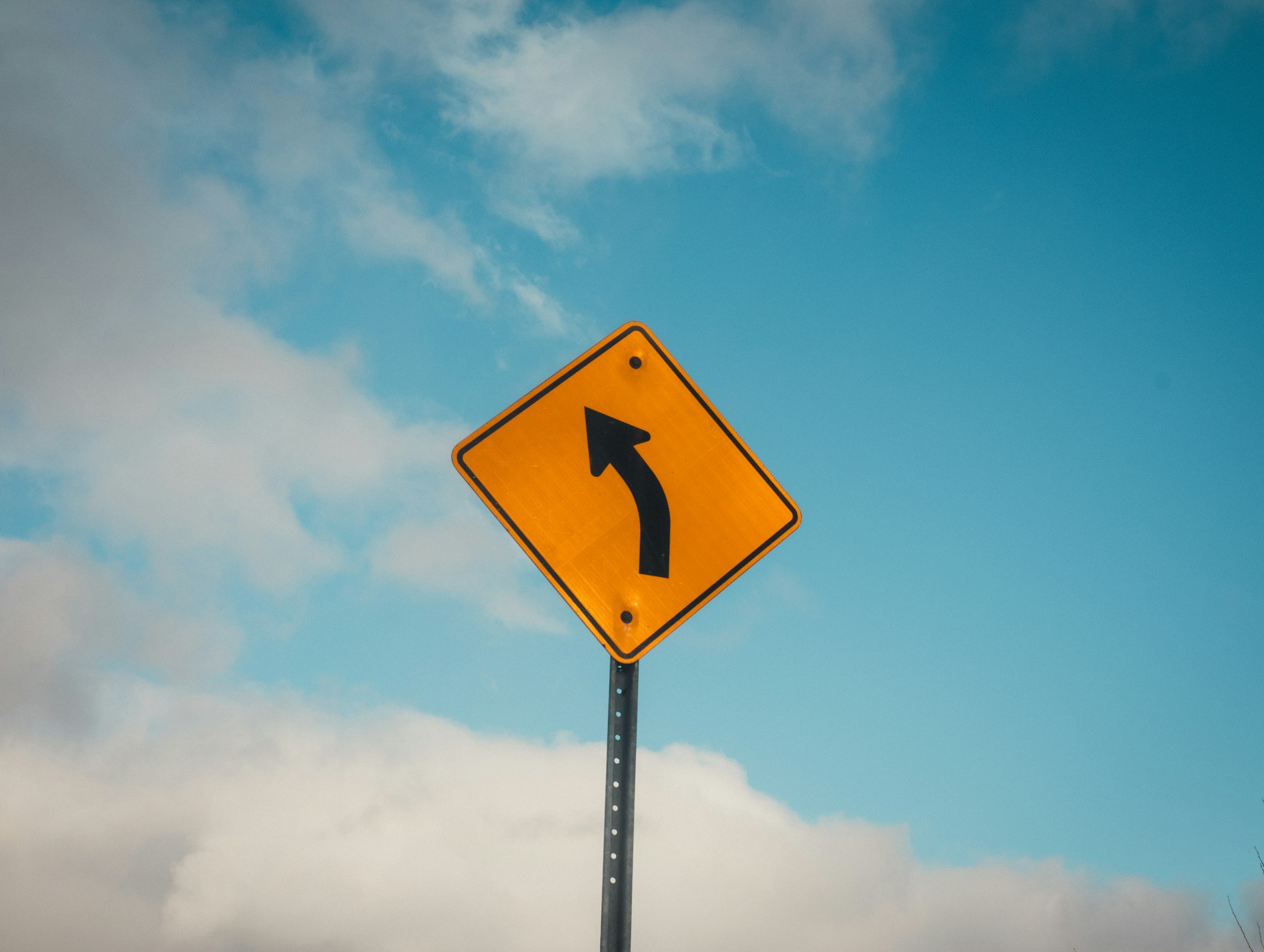 Yellow road sign indicating a sharp left turn
