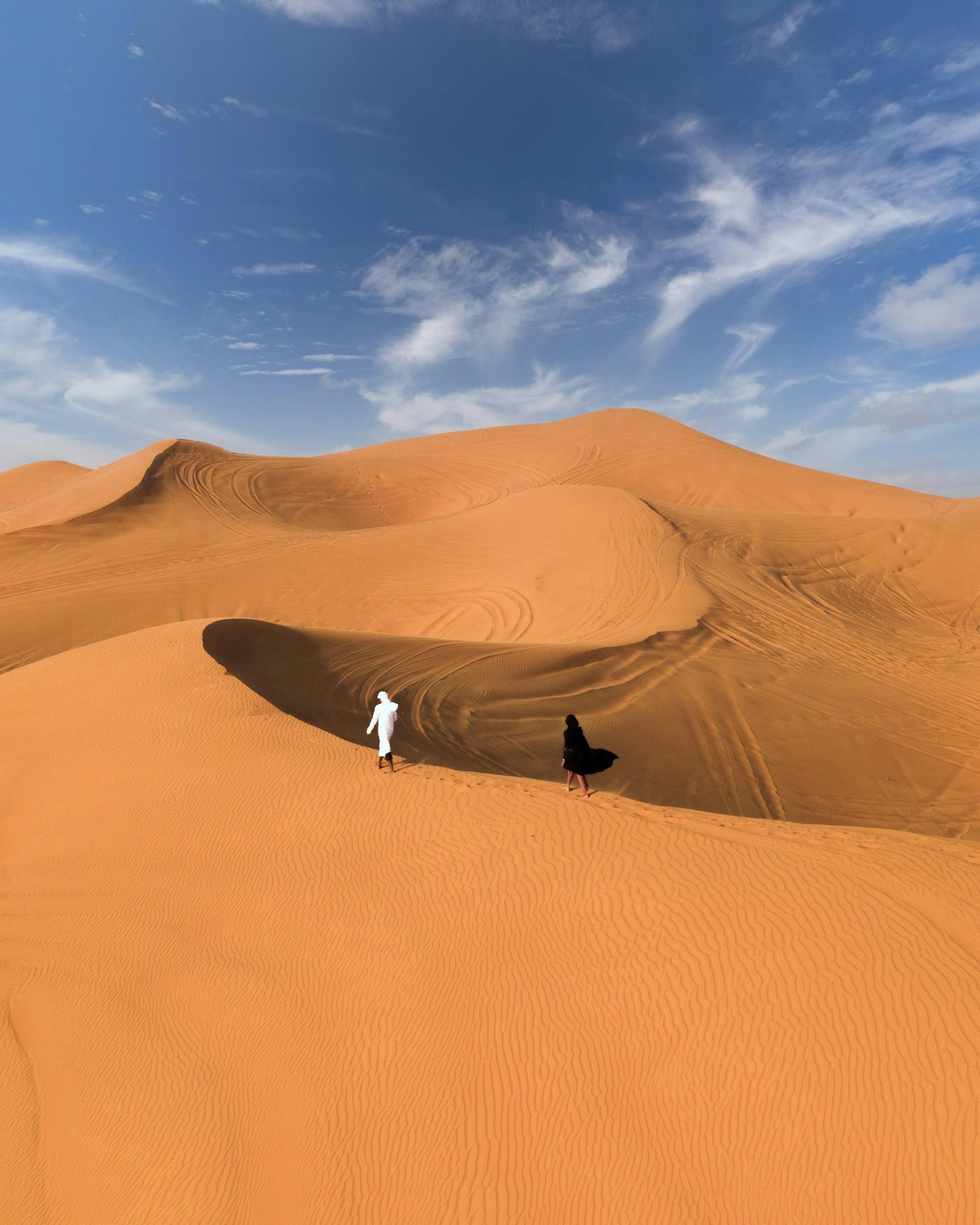 A lone figure standing on desert sand under a blue sky