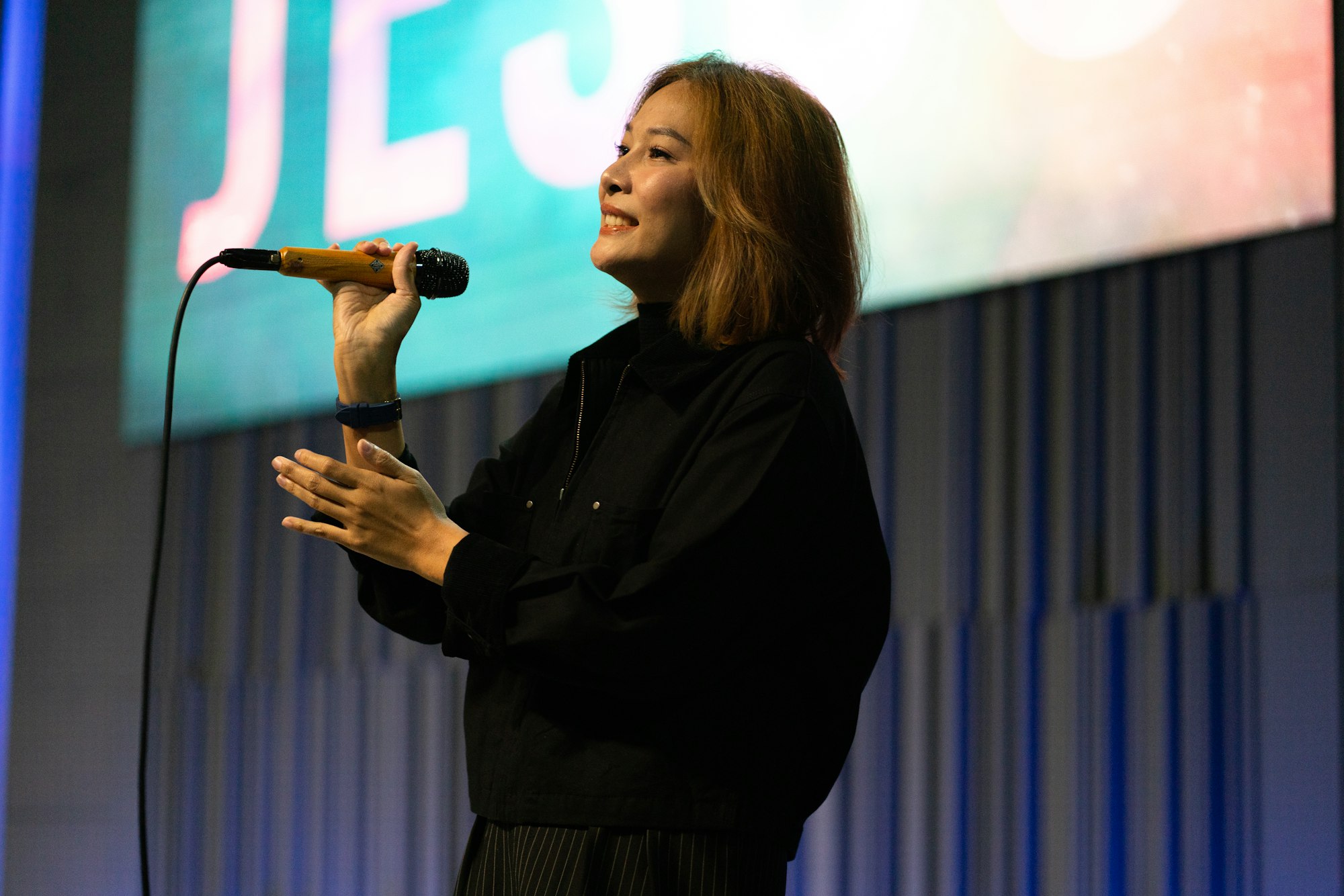 A woman sings into a microphone on stage