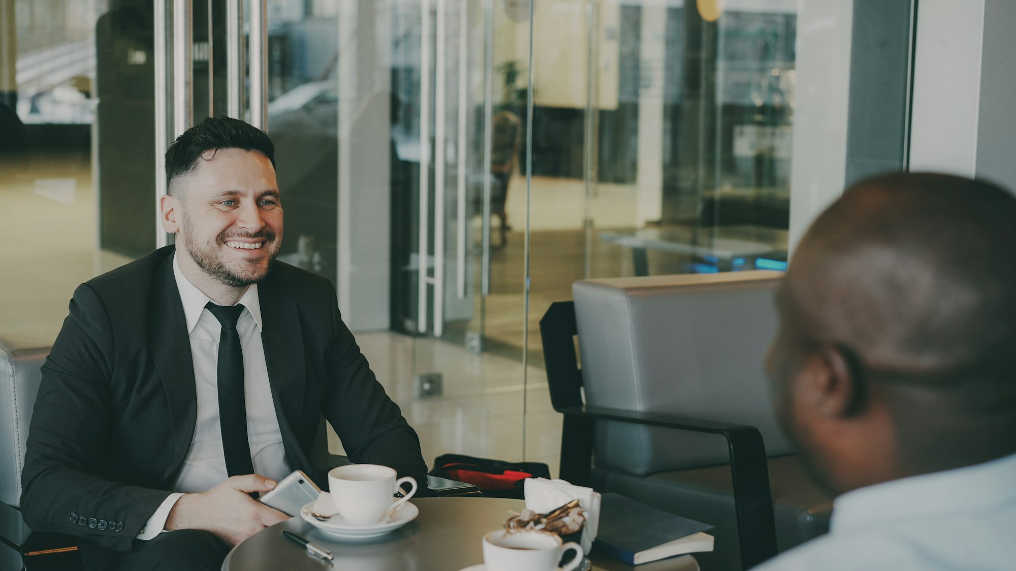 Two businessmen smiling and talking at a cafe table