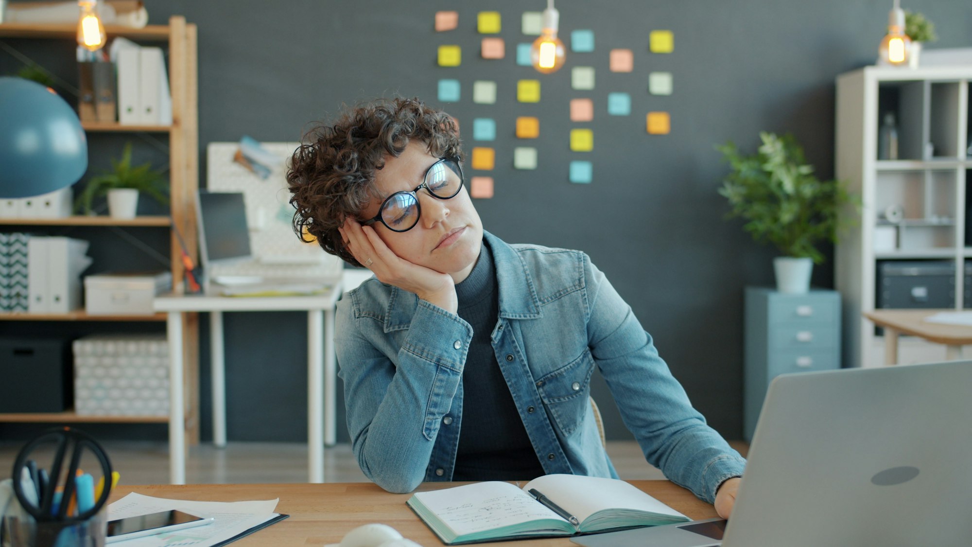 Tired person resting head on hand at desk.