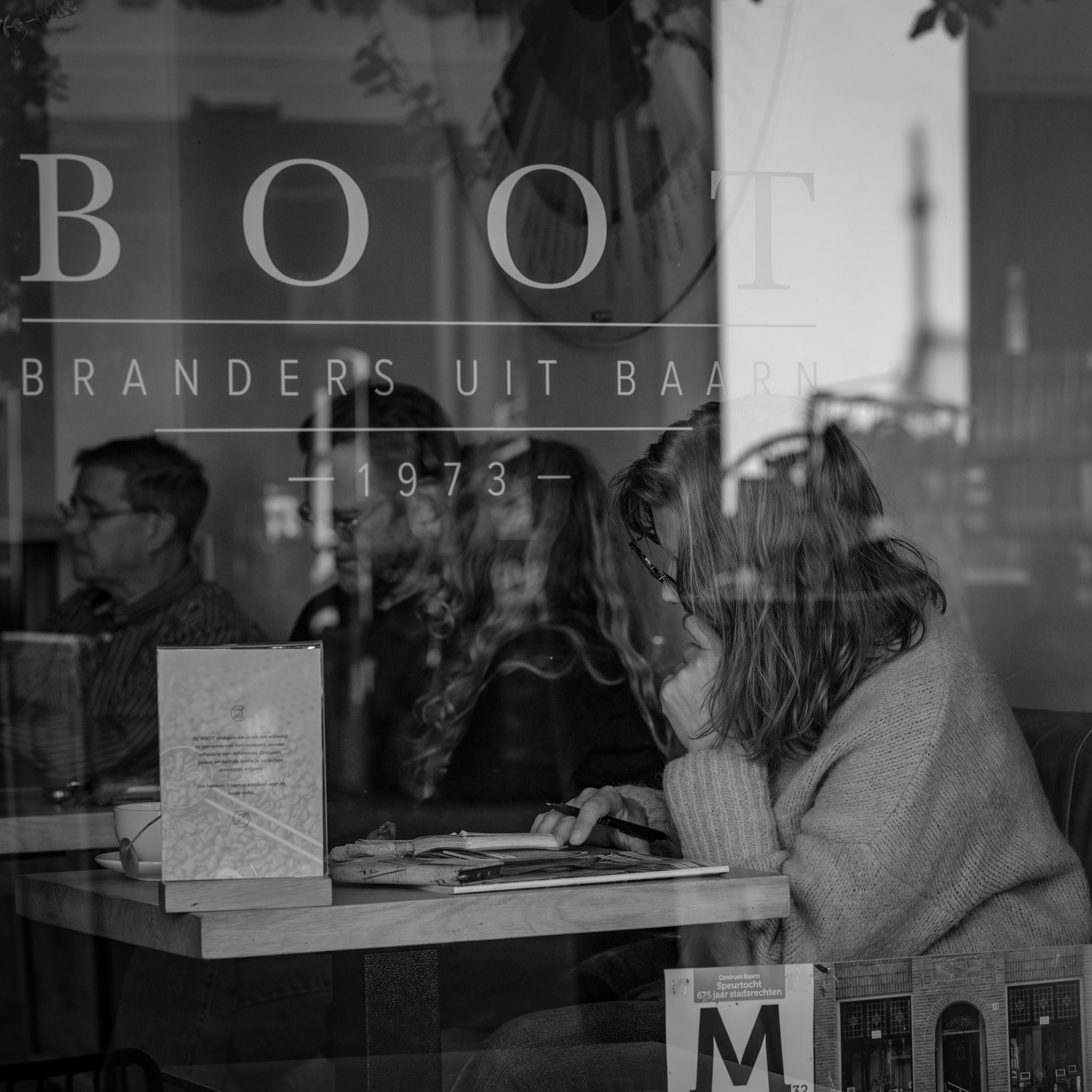 People sit at tables inside a cafe window.
