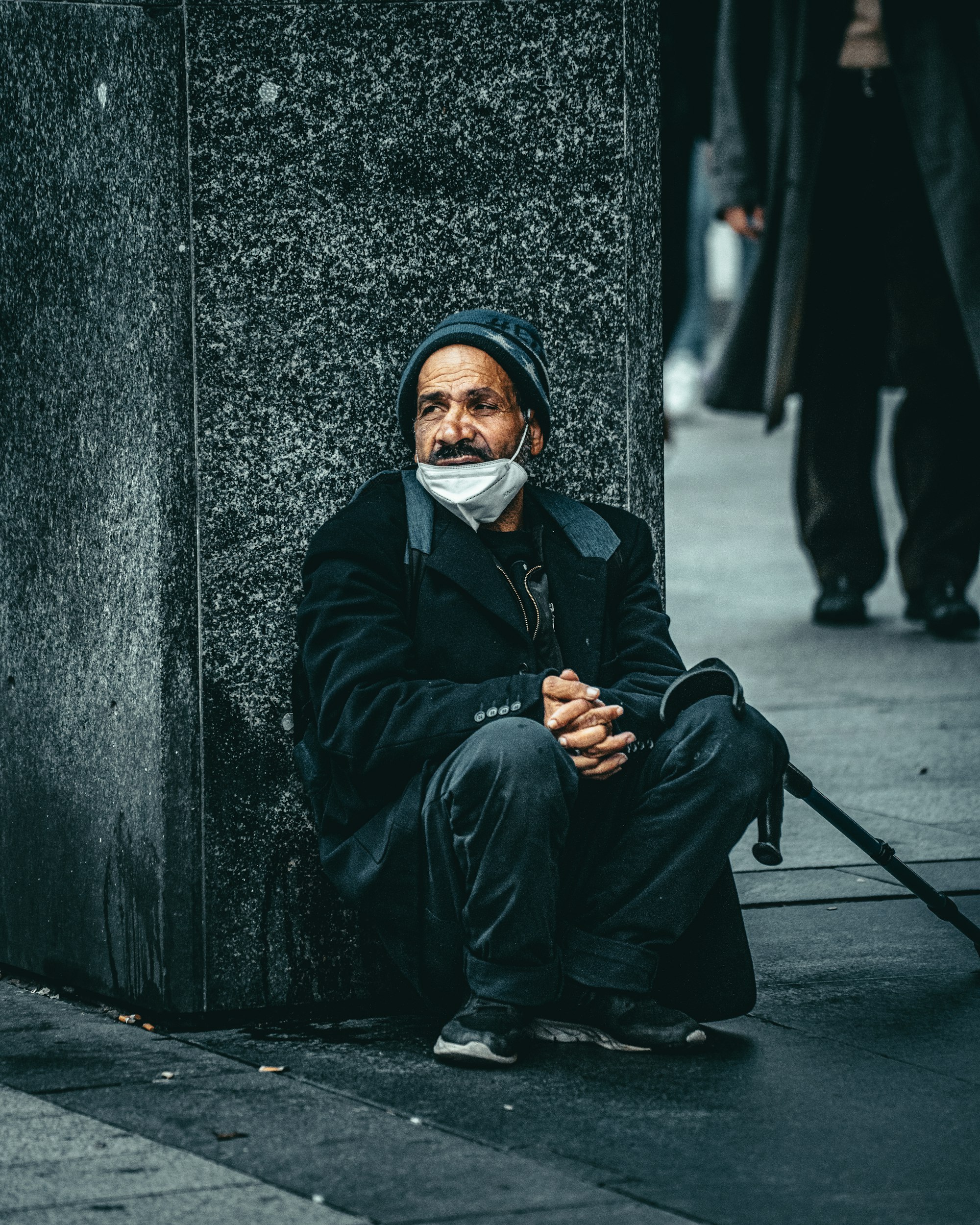 Man in black jacket and white mask sitting on concrete wall