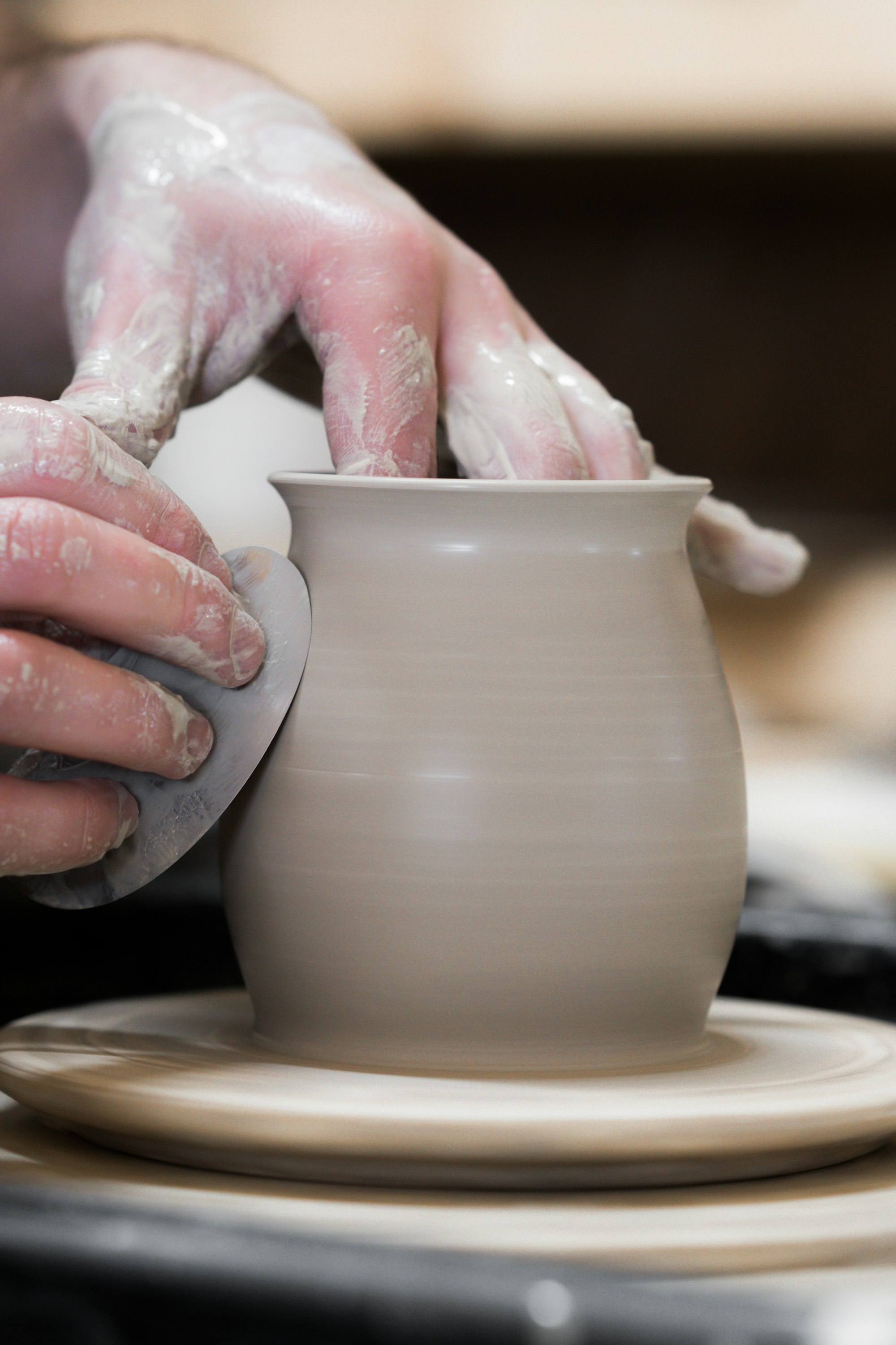 A person's hands holding a finished white clay pot