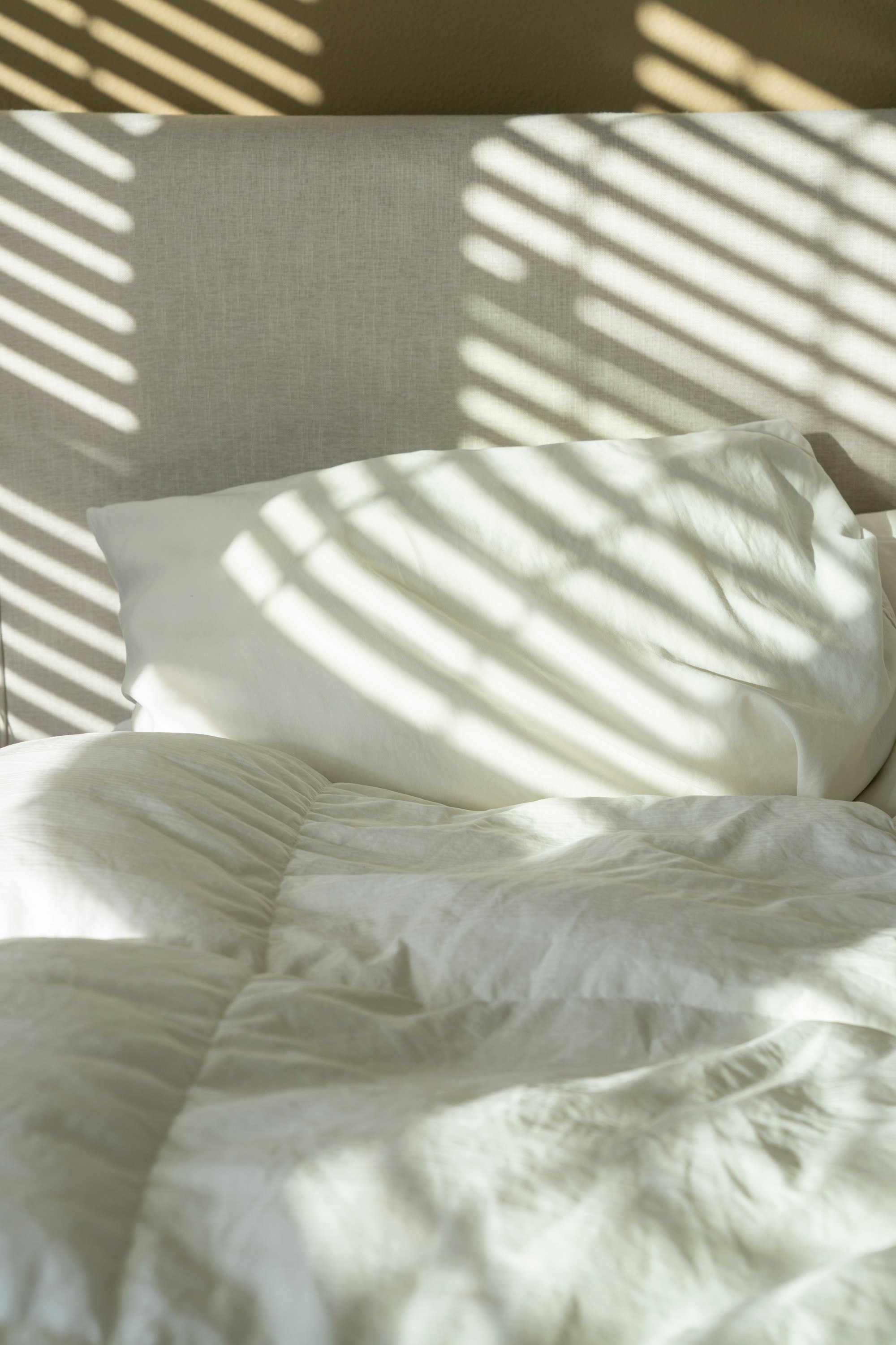 A bed with white sheets and pillows in morning light