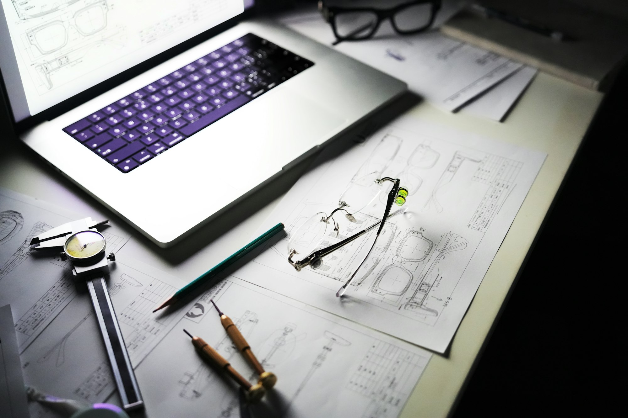 Desk with laptop, blueprints, and drafting tools