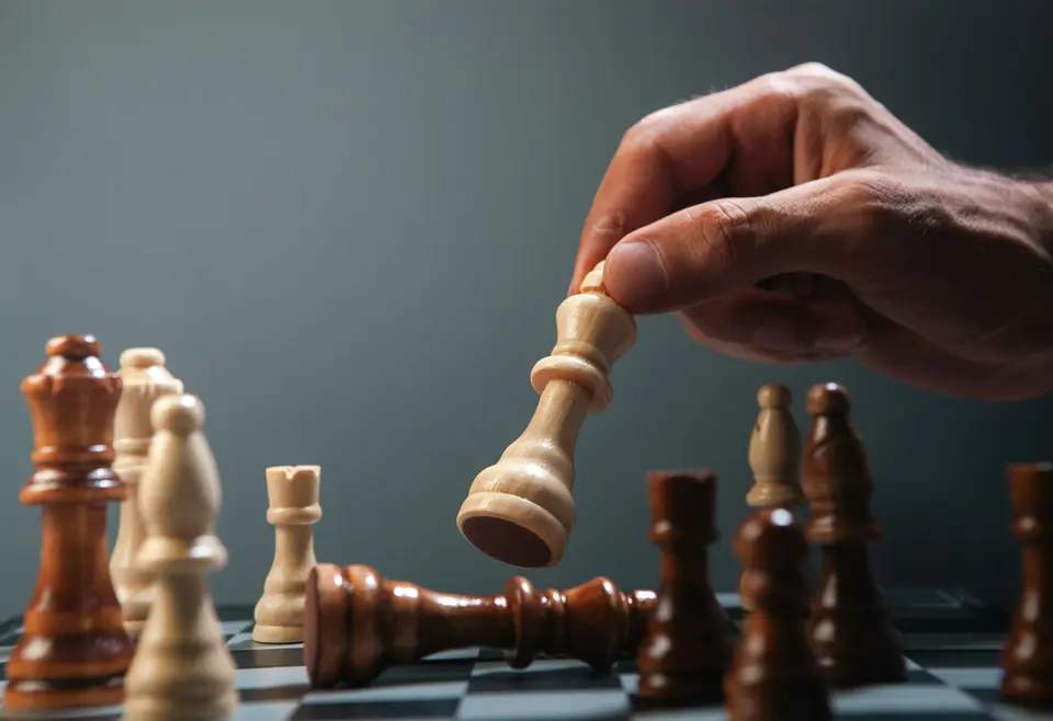 Hand moving a white chess piece over fallen king