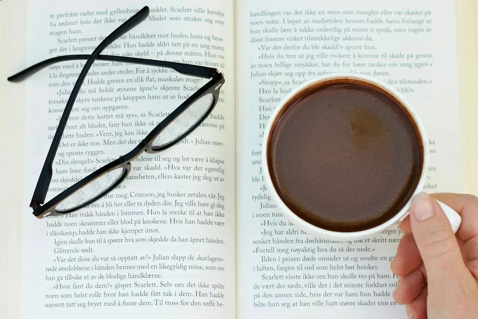 Person holding a cup of coffee in front of an open book