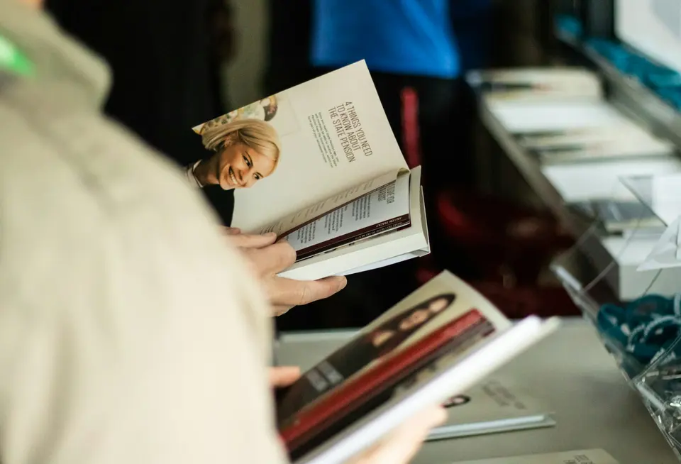 Person holding an open book beside a table of books