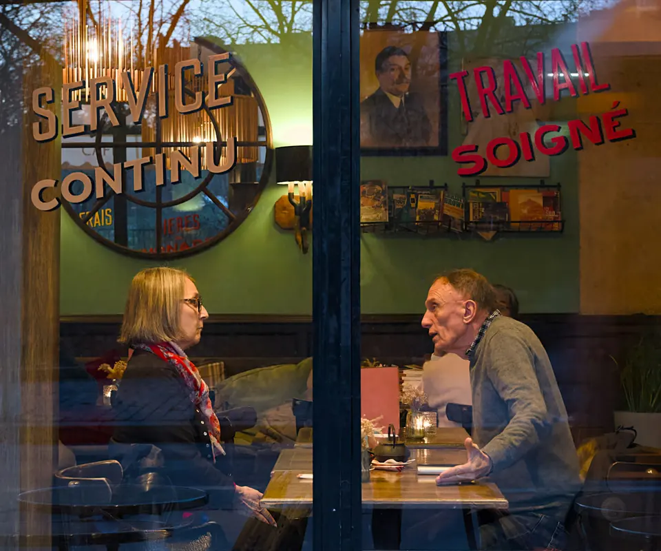 Two people seated at a cafe table, seen through a window