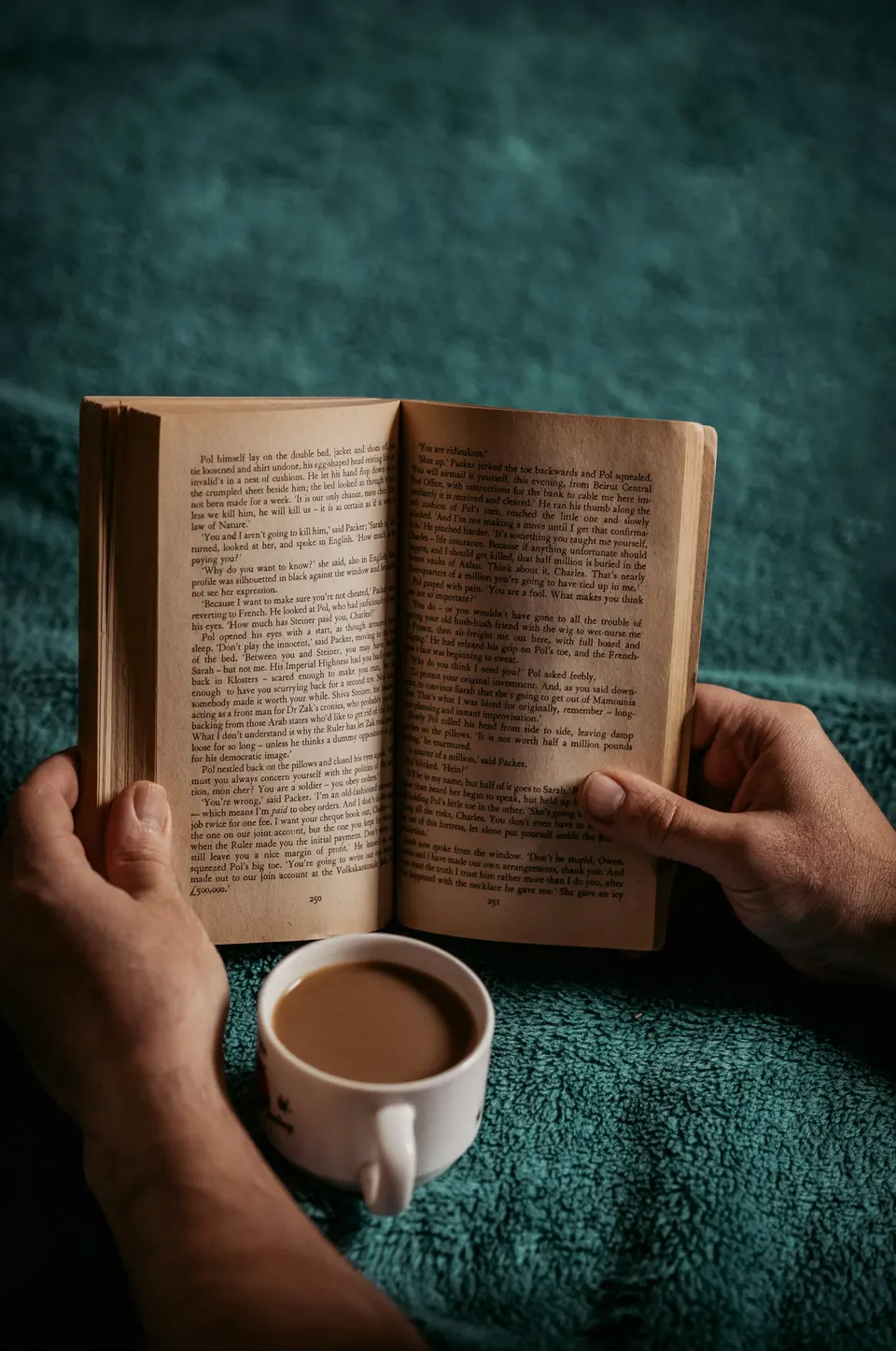 Hands holding an open book with a cup on a textured blanket