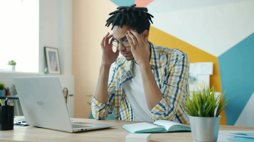 Man holding his head at desk with laptop, struggling with mental health