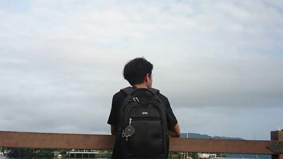Person with a backpack facing a cloudy horizon