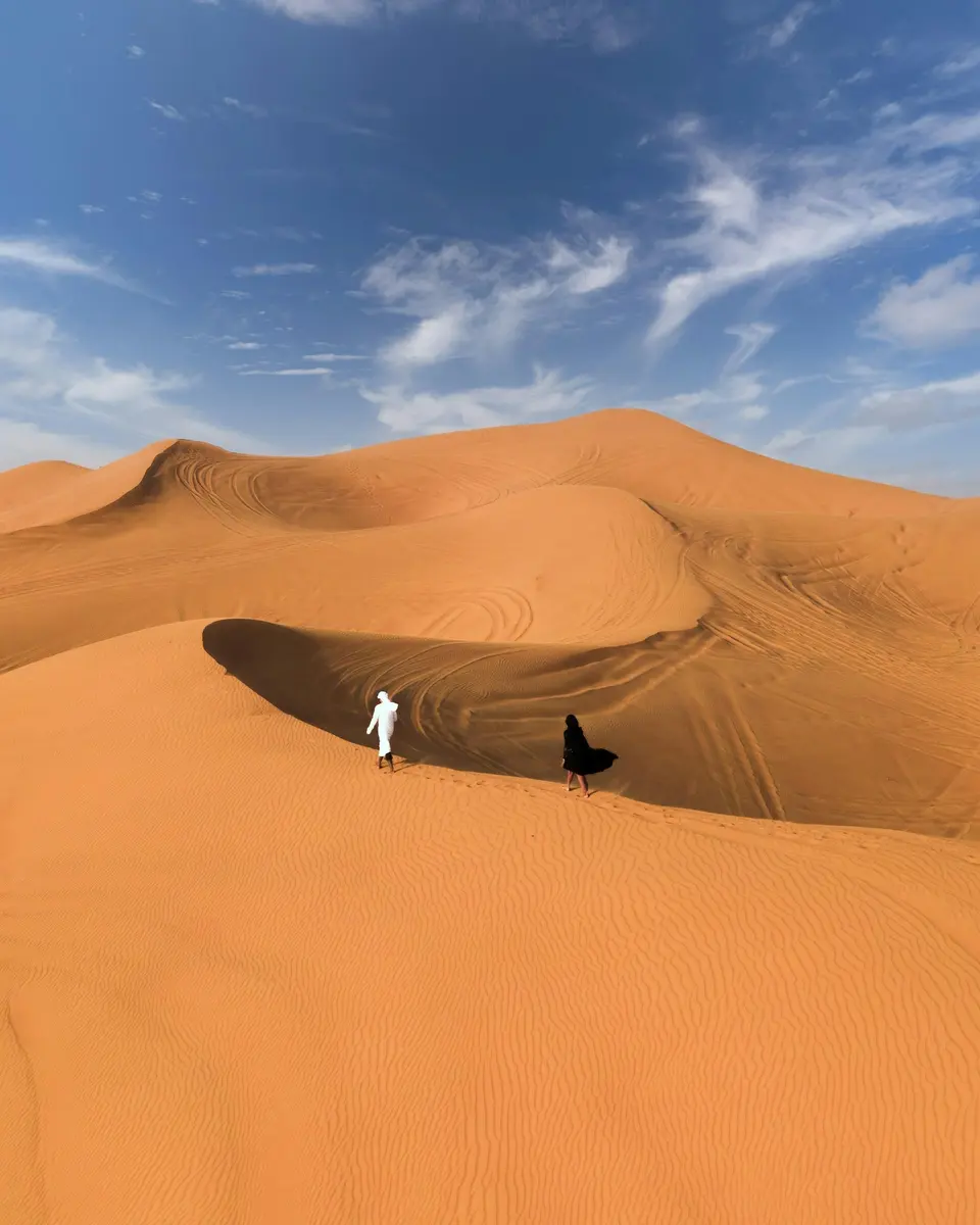 A lone figure standing on desert sand under a blue sky