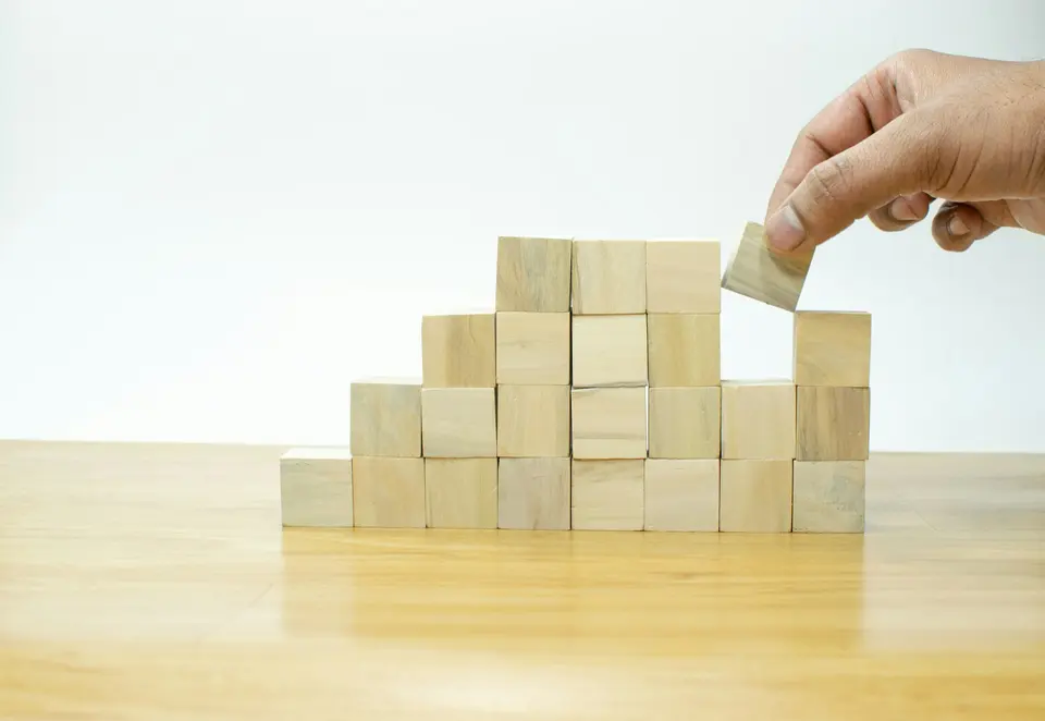 A hand placing a wooden block onto a growing stack