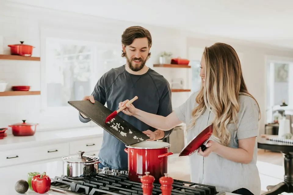Two people cooking at a stove with red pots