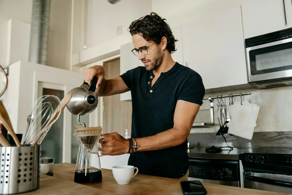 Man pouring morning coffee in a kitchen with a French press