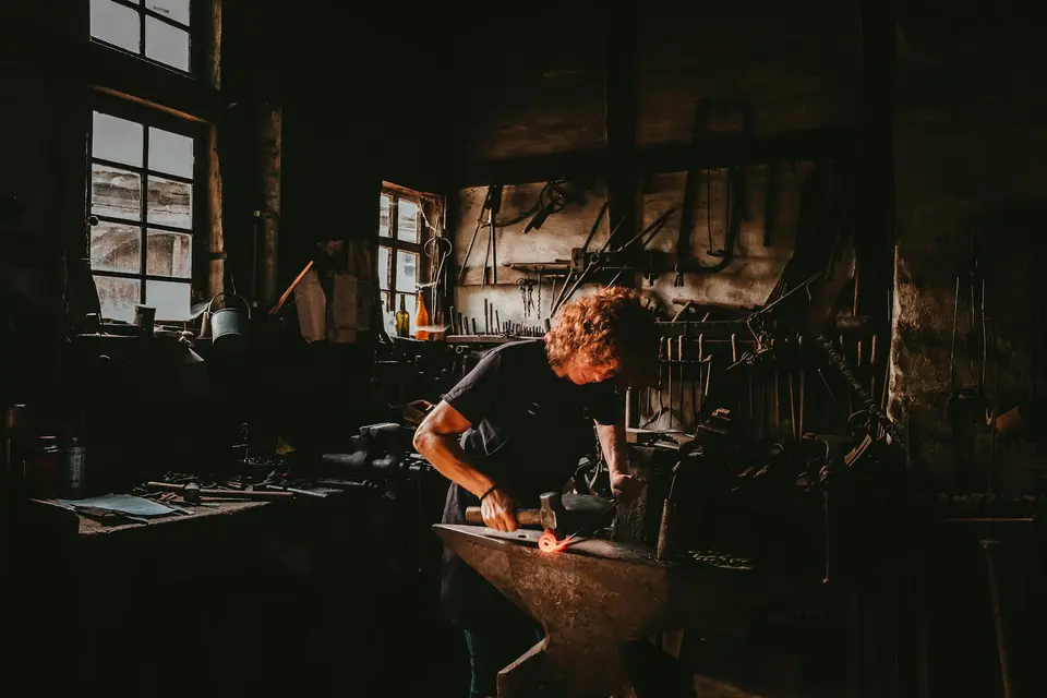 Man hammering metal on an anvil inside a workshop