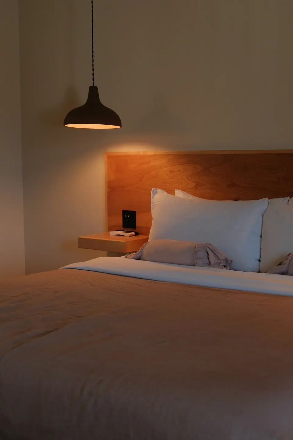 Made bed with white pillows beneath a lit pendant lamp