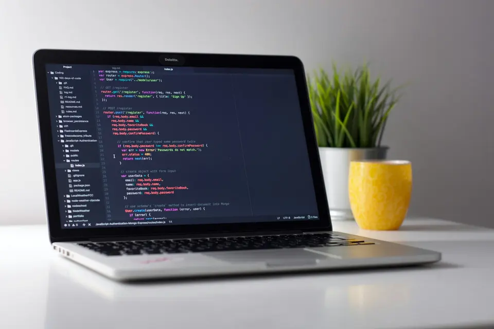 A laptop displaying code beside a yellow mug and a plant