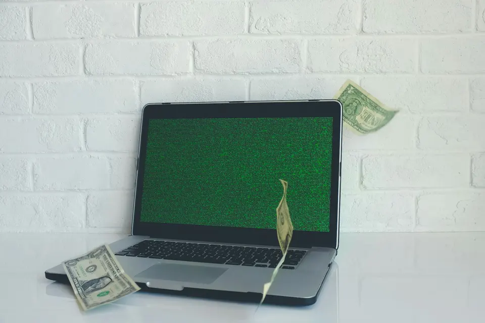 Hands holding crumpled dollar bills, scattered on dark surface