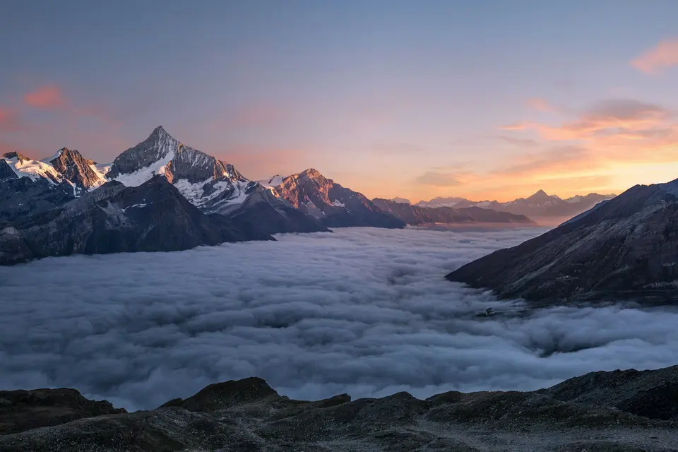 Snow-covered mountain peaks above a layer of clouds at sunset