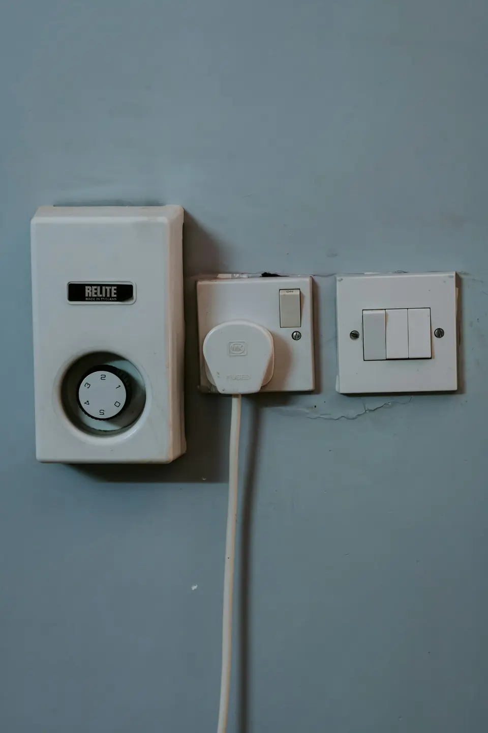 A wall-mounted dial beside a power plug and switches